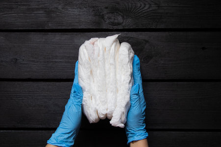 Female hands in medical gloves holding white disposable adult diaper pants on black wooden...