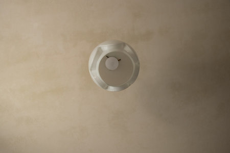 Ceiling lamp with a white round shade and a light bulb in a room with old repairs and light plaster...