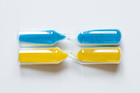 Hourglass with yellow and blue sand, lying horizontally on a white background