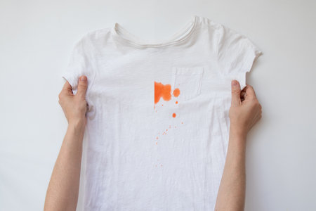Girl shows white t-shirt before and after washing with orange paint stain on white backgroundの写真素材