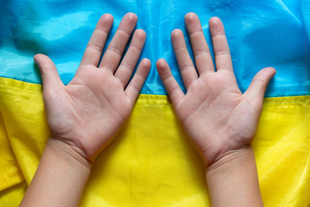 The open palms of a little boy lying on the background of the flag of Ukraine as a symbol of childhood, peace, future and national identityの写真素材