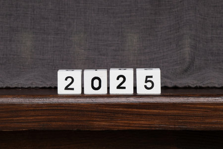 White cubes with black numbers lined up to represent the year 2025, cubes standing on a wooden table...