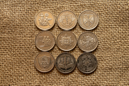Nine Ukrainian commemorative coins of 10 hryvnia with symbols of various units on fabric