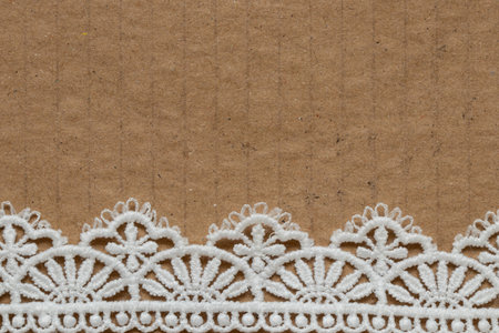 A piece of brown cardboard with white lace at the bottom as a background or texture for decoration, suitable as a decorative templateの写真素材