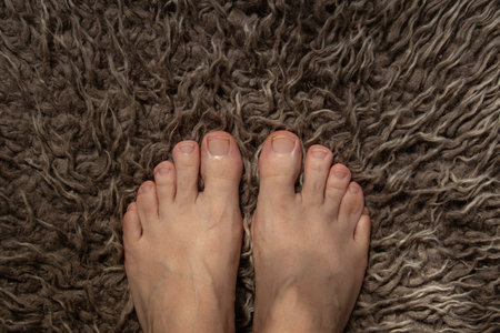 Female feet standing on brown fluffy carpet on the topic of feet and foot care and healthの写真素材