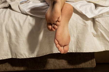 Little boy's dirty bare feet hanging off the bed in the bedroom in the apartment when he sleepsの写真素材