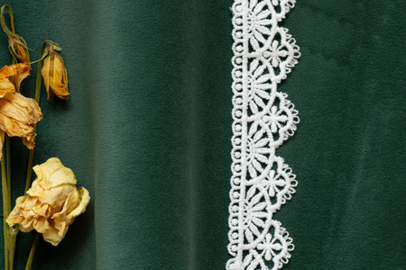 A sprig of dried flowers lying on emerald colored wavy velour and a ribbon of lace as a texture or...