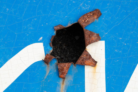 A damaged blue road sign with a large punctured hole and rust and peeling paint around it during the shelling of Ukraineの写真素材
