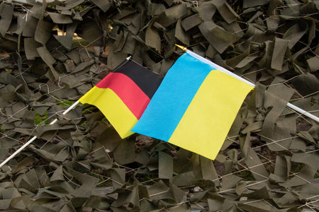 Flags of Germany and Ukraine attached to a camouflage military net made of green fabric ribbons as support for the army and unity with Ukraineの写真素材