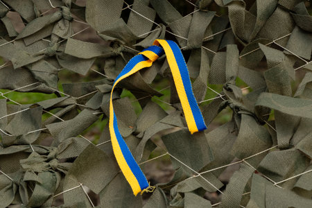 Military camouflage net made of green fabric tapes and Ukrainian flag tape tied to the net as a background, war in Ukraineの写真素材