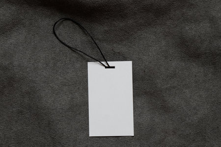 White empty tag on rope lies on gray fleecy fabric as a mockup for design close-upの写真素材