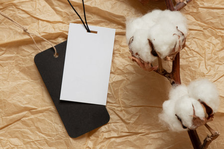 Black and white empty tags on ropes lie on brown crumpled paper and a sprig of dry cotton as a...