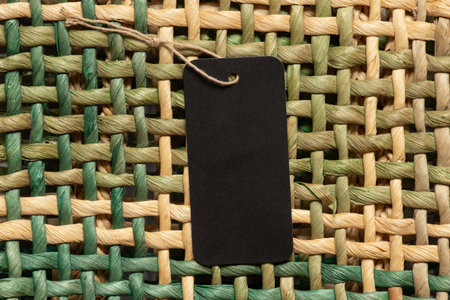 Black empty tag on a rope lies on a wicker straw background as a mockup for design