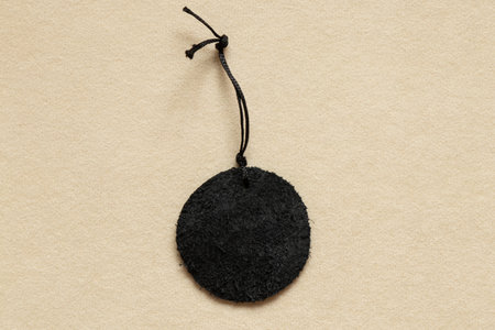 A round piece of black shaggy leather with a rope and lying on a beige background close-up