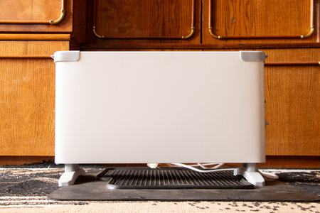 An electric convector heater installed on the floor of a residential apartment, against a backdrop of wooden furniture in Ukraineの写真素材