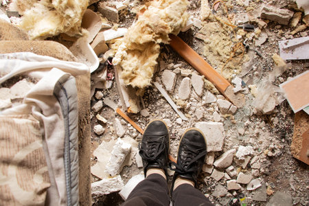 Rubble clearing after a drone explosion under the window of a multi-story building, with shattered windows and spilled belongings during the war in Ukraineの写真素材