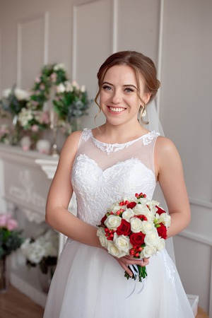 Brown-haired bride with classic wedding hairstyle, smiling taking wedding bouquet in her hands.の写真素材