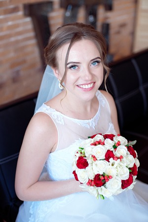 Brown-haired bride with classic wedding hairstyle, smiling taking wedding bouquet in her hands.の写真素材