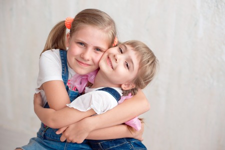 Two adorable little sisters laughing and hugging each other in studio. Great sister's love.の写真素材