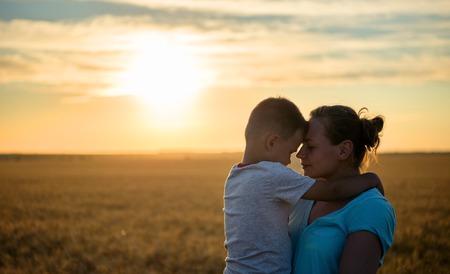 Happy mother kisses on the forehead baby holding on a wheat field in sunlight, family in a wheat field On the Sunset.の写真素材