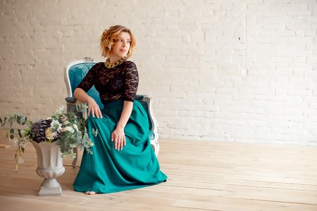 Image of elegant girl sitting in retro style armchair. Redhaired curly young model.の写真素材