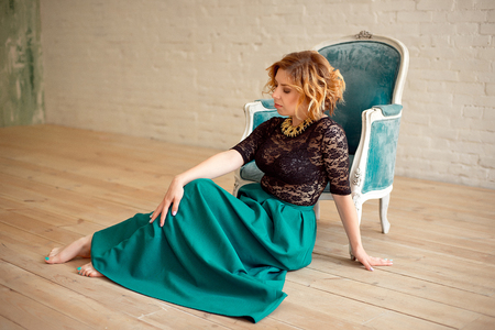 Image of elegant girl sitting in retro style armchair. Redhaired curly young model.の写真素材