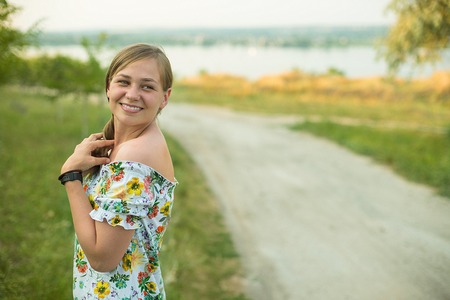 Half length portrait of charming positive woman dressed in long white summer dress happy smiling in sunset background.の写真素材