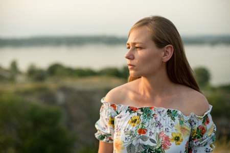 Half length portrait of charming positive woman dressed in long white summer dress happy smiling in sunset background.の写真素材