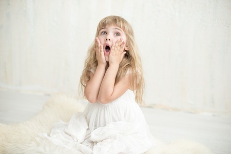Portrait of pretty little girl in white dress , she is surprised and put her hands on cheeks.