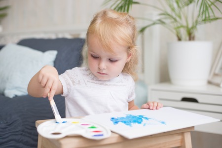 Happy little girlpainting with gouache and watercolor paints on the easel indoors.の写真素材