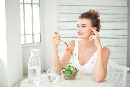 Portrait of a young smiling woman eating a fresh salad in white room.の写真素材