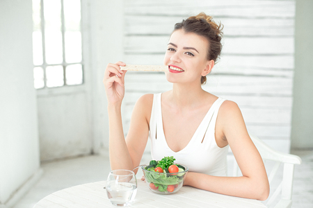 Portrait of a young healthy woman eating a crispbread in white room.の写真素材