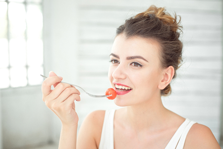 Close up portrait of attractive healthy young woman eating green salad indoors.の写真素材