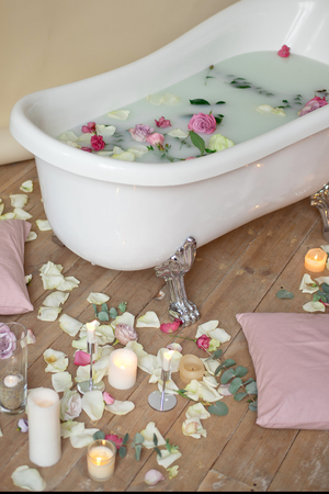 Romantic bubble bath with roses and candles for aroma therapy. White antique freestanding bath and flower petals on the floor and in soapy water, viewed from high angleの写真素材