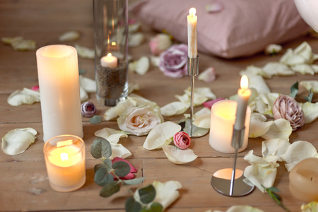 Spa, health, beauty and wellness concept with rose petals scattered around burning candles on a wooden floor in a high angle viewの写真素材