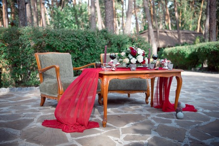 Romantic table for two with fresh flowers and candles on an outdoor garden patio set with red wine, fresh figs, pomegranate and French macaronsの写真素材