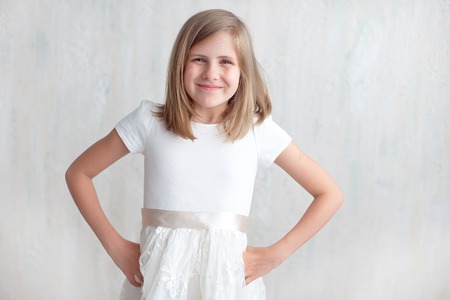 Portrait of pretty little girl in white dress with arms akimbo indoor.の写真素材