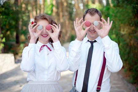 Young couple in white shirts holding colored macarons on the eyesの写真素材