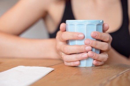 Female hands holding a cup of coofee on the wooden tableの写真素材