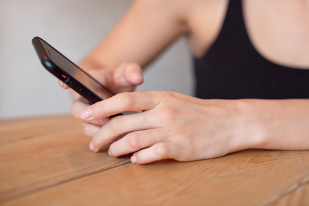 Female hands holding cell phone at the wooden table.の写真素材