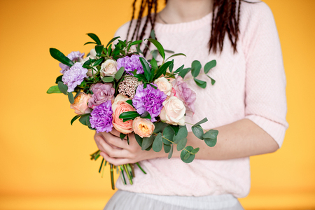 Close-up Beautiful woman with dreadlocks hairstyle holding a bouquet of flowers indoors.の写真素材
