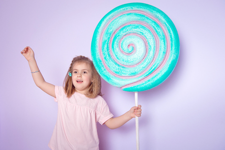 Little girl sitting in colorful room around big toyful candies, donut, lollipopの写真素材