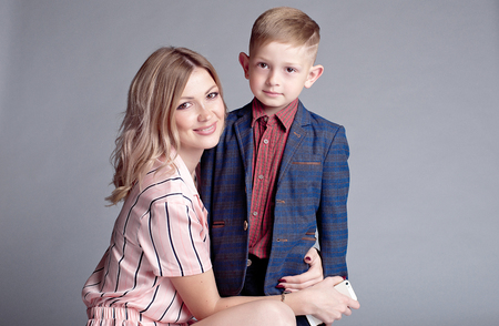 woman hugging cute little boy with modern hairstyle in blue jacket happy smiling indoorsの写真素材