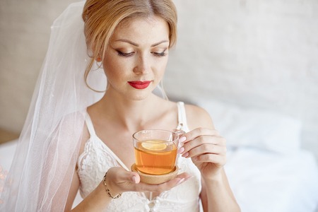 Close-up blonde bride drinking morning tea in lingerie and veilの写真素材