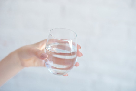 Female hands holding a clear glass of water.