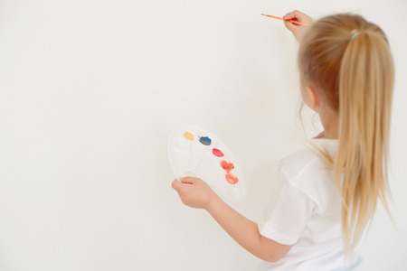 Cute little girl painting on wall in empty roomの写真素材
