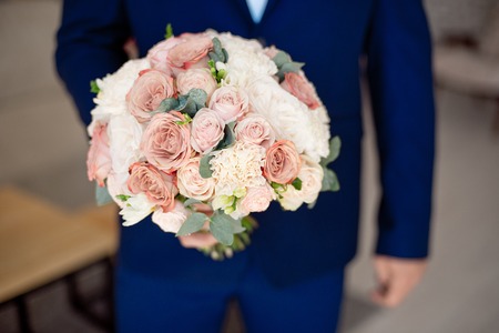 Close-up shot of a man holding a wedding bouquet in front of him wearing in blue suitの写真素材