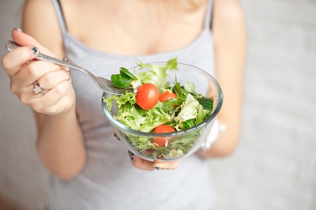 Close-up rear view woman holding bowl of fresh vegetable salad holding fork in hand.の写真素材