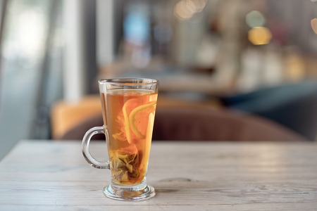 Clear glass cup of tea on table in cafe interior with blurred color backgroundの写真素材