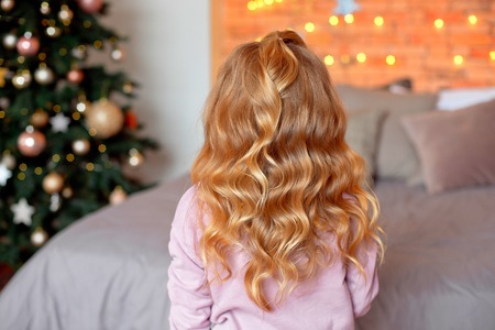 Rear view of girl hairstyle. Little girl standing with her back and looking at the christmas tree.Christmas and New Year conceptの写真素材